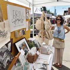 a woman standing next to a table with pictures and other items on it at an outdoor market