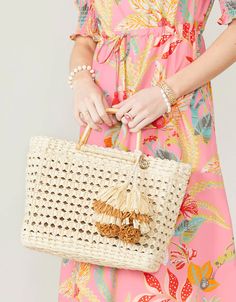 a woman in a pink dress holding a white purse with tassels on it