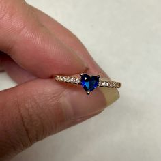 a person's hand holding a ring with a blue heart shaped diamond on it