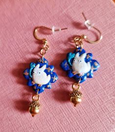 two blue and white earrings with sheeps on them are sitting on a pink surface