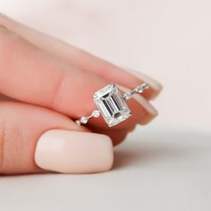 a woman's hand holding an engagement ring with a large emerald stone in it