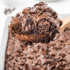 a spoon full of chocolate cake batter being lifted from a casserole dish with a wooden spoon