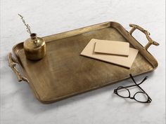 a brass tray with glasses and a teapot on it next to a pair of reading glasses