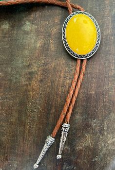 This awesome bolo tie has a southwestern design and yellow stone centerpiece.  The cord is genuine leather. All the stones will vary slightly. Our bolos pair nicely with many of our belt buckles! They make wonderful gifts.    The western bolo tie rope length is 39'' ; charm agate stone pendant size is 1 3/4'' x 1 1 /2'' Adjustable Yellow Lariat Jewelry, Brown Concho Bolo Tie Lariat, Brown Concho Bolo Ties Lariat, Brown Concho Bolo Tie, Western Bolo Tie, Mens Necklace, Southwestern Design, Tie Gifts, Bolo Tie