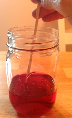 a person is holding a stick in a jar filled with liquid