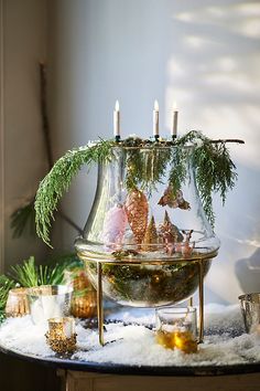 a glass vase filled with christmas decorations and candles on top of a snow covered table