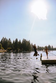 two people jumping off a dock into the water with trees in the background on a sunny day