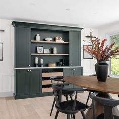 a dining room table and chairs in front of an open cabinet with shelves on the wall