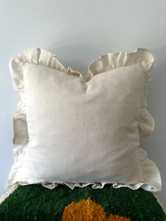 a white pillow sitting on top of a green and yellow rug with ruffled edges