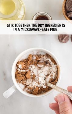 a person holding a spoon in a mug filled with chocolate and marshmallows