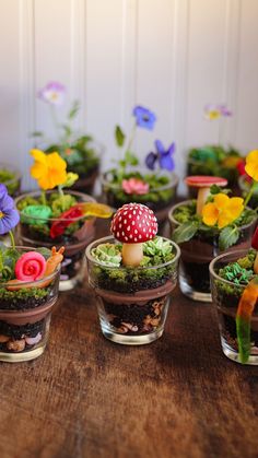 small glass vases filled with miniature plants and mushrooms on a table top, decorated with fake flowers