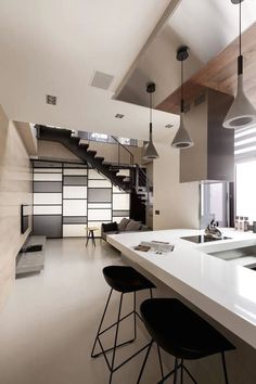 View of a stylish narrow great room with a modern design. Pendant lights hang above the dining-space countertop at right, while we see a cozy living room space in the distance, standing beneath a checkered panel wall and set of open-design stairs. Foscarini Aplomb, Transitional Home Decor, Design Blogs, Occasional Tables, Top Furniture, Contemporary Apartment, Green Home Decor, Home Decor Online, Home Modern