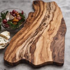 a wooden cutting board sitting next to a bowl of grapes and cheese