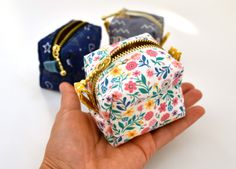 a hand holding two small purses on top of a white table next to each other