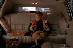 a young boy sitting in the back seat of a car eating pizza