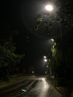 an empty street at night with lights shining on the road and trees in the background