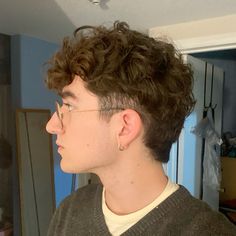 a young man with curly hair and glasses looking off into the distance while standing in front of a mirror