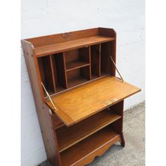 an old fashioned wooden desk with shelves and drawers on the top, against a white wall