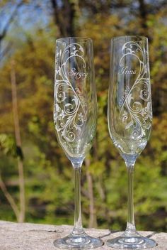 two wine glasses sitting next to each other on top of a stone slab in front of trees