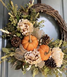 a wreath with pumpkins, flowers and pine cones is hanging on the front door