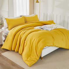 a bed with yellow sheets and pillows in a white room next to a lamp on a table