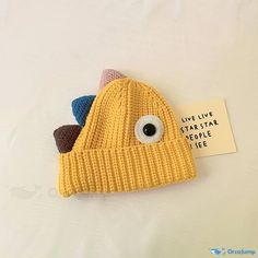 a yellow knitted hat with an eye on it and a tag attached to the side