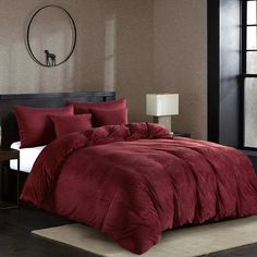 a bed with red comforter and pillows in a room next to a window,