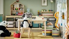 two stuffed panda bears sitting at a table in a playroom with toys and books