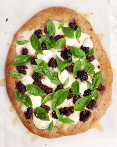 a pizza topped with blackberries and basil leaves