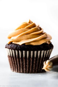 a chocolate cupcake with frosting and caramel icing on top, next to a knife