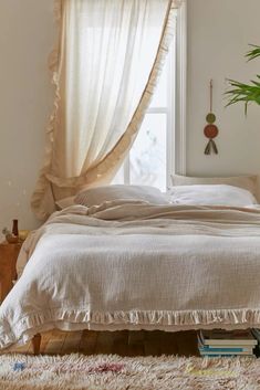 a white bed sitting under a window next to a wooden table with a potted plant on top of it