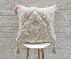 a white pillow with tassels sitting on top of a stool next to a brick wall