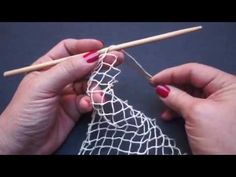 two hands holding knitting needles over a piece of white netted material with yarn on it