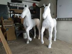 two paper mache horses standing next to each other in a room filled with boxes