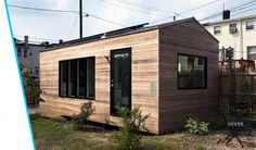 a small wooden house sitting on top of a lush green field next to tall buildings