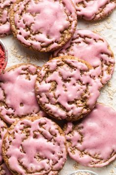 cookies with pink icing and sprinkles on a white surface next to a bowl of powdered sugar