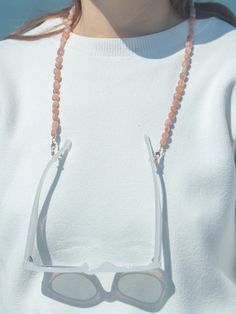 a woman wearing sunglasses and beaded necklace with beads on her neck, standing in front of the ocean