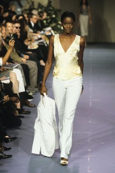 a model walks down the runway in white pants and a yellow top with an open back