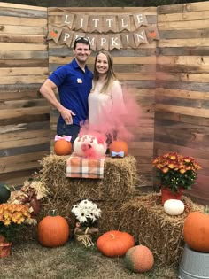 a man and woman standing in front of hay bales with pumpkins