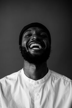 a black and white photo of a man laughing with his eyes closed while wearing a hat