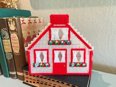 a red and white house sitting on top of a book shelf next to two books