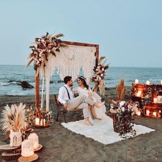 a man and woman sitting on top of a beach next to an arch covered in candles