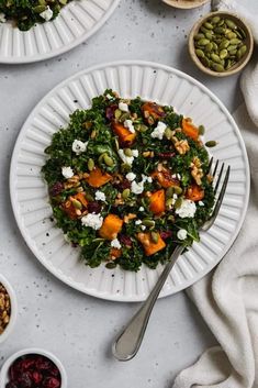 two white plates filled with salad next to bowls of nuts