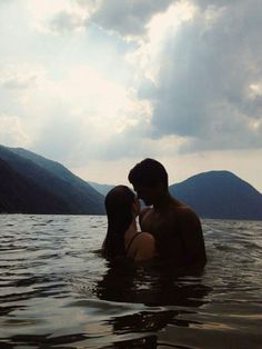 two people are in the water with mountains in the backgrouds behind them