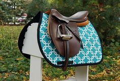 a brown and blue horse saddle sitting on top of a white wooden stand in the grass