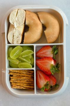 a lunch box with fruit, crackers and pretzels on the side for two people to eat