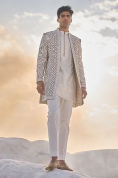 a man standing on top of a snow covered hill wearing a white suit and tie