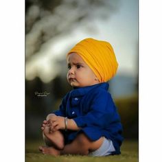 a baby wearing a yellow turban sits on the ground and looks off to the side