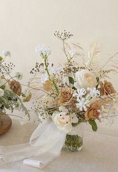 two vases filled with flowers and greenery on a white tablecloth covered table