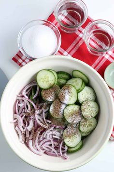 a white bowl filled with sliced cucumbers next to two glasses of water and a red checkered table cloth